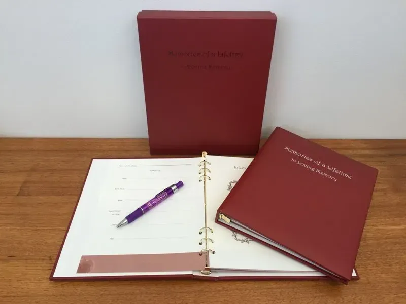 A purple pen sits on a wooden table next to a red binder