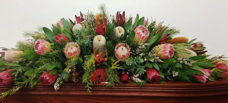 A large bouquet of flowers is sitting on top of a wooden coffin.