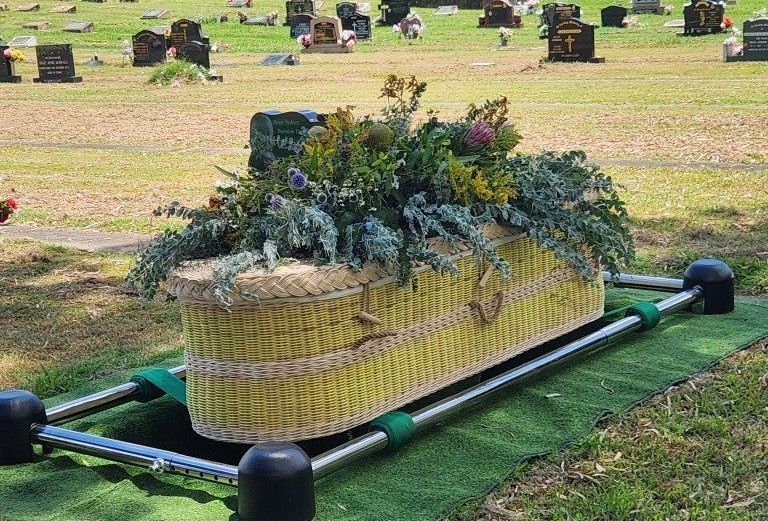 A yellow coffin with flowers on it is in a cemetery.