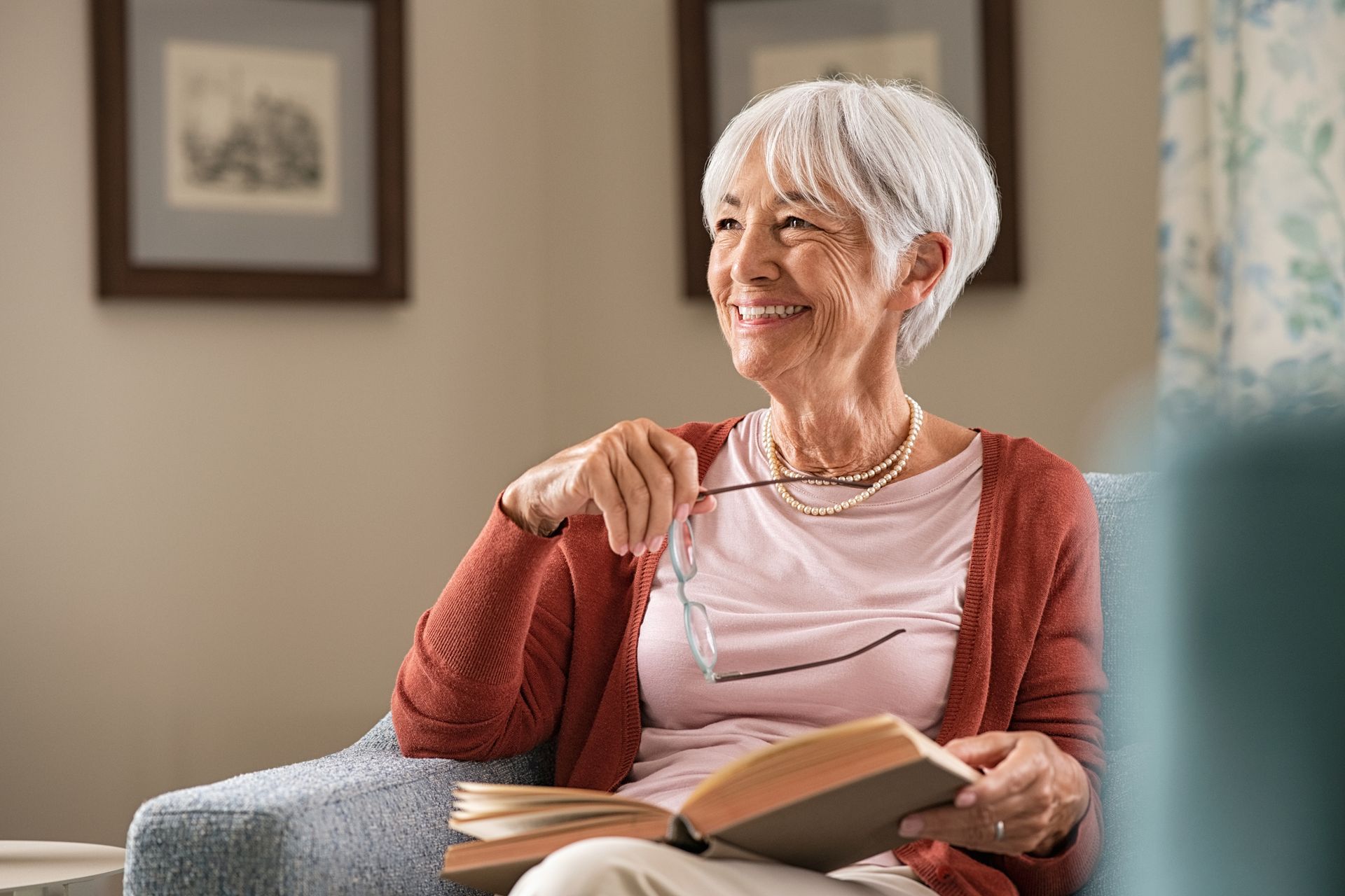 An elderly woman is sitting in a chair reading a book.
