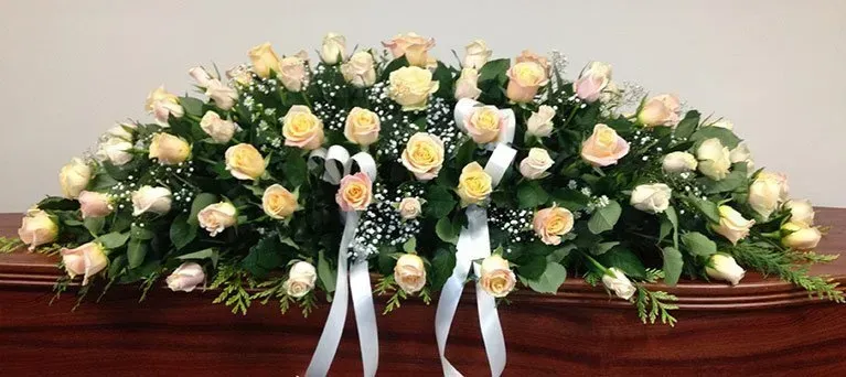 A coffin covered in flowers and ribbons is sitting on a wooden table.