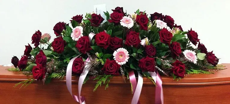 A coffin is decorated with red roses and pink ribbons