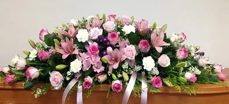A casket covered in pink and white flowers and greenery.