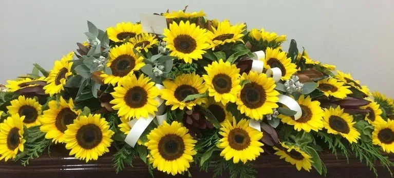 A coffin covered in sunflowers and greenery is sitting on a table.