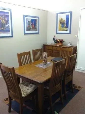 A dining room with a wooden table and chairs and paintings on the wall.