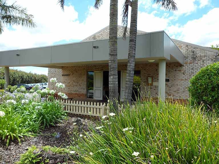 A large brick building with a white picket fence and palm trees in front of it.