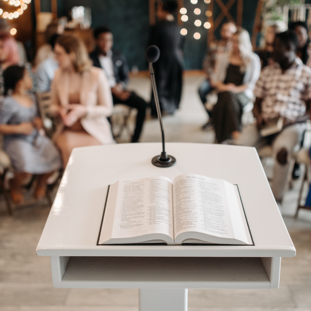 A man with a beard is giving a speech at a podium in a church.