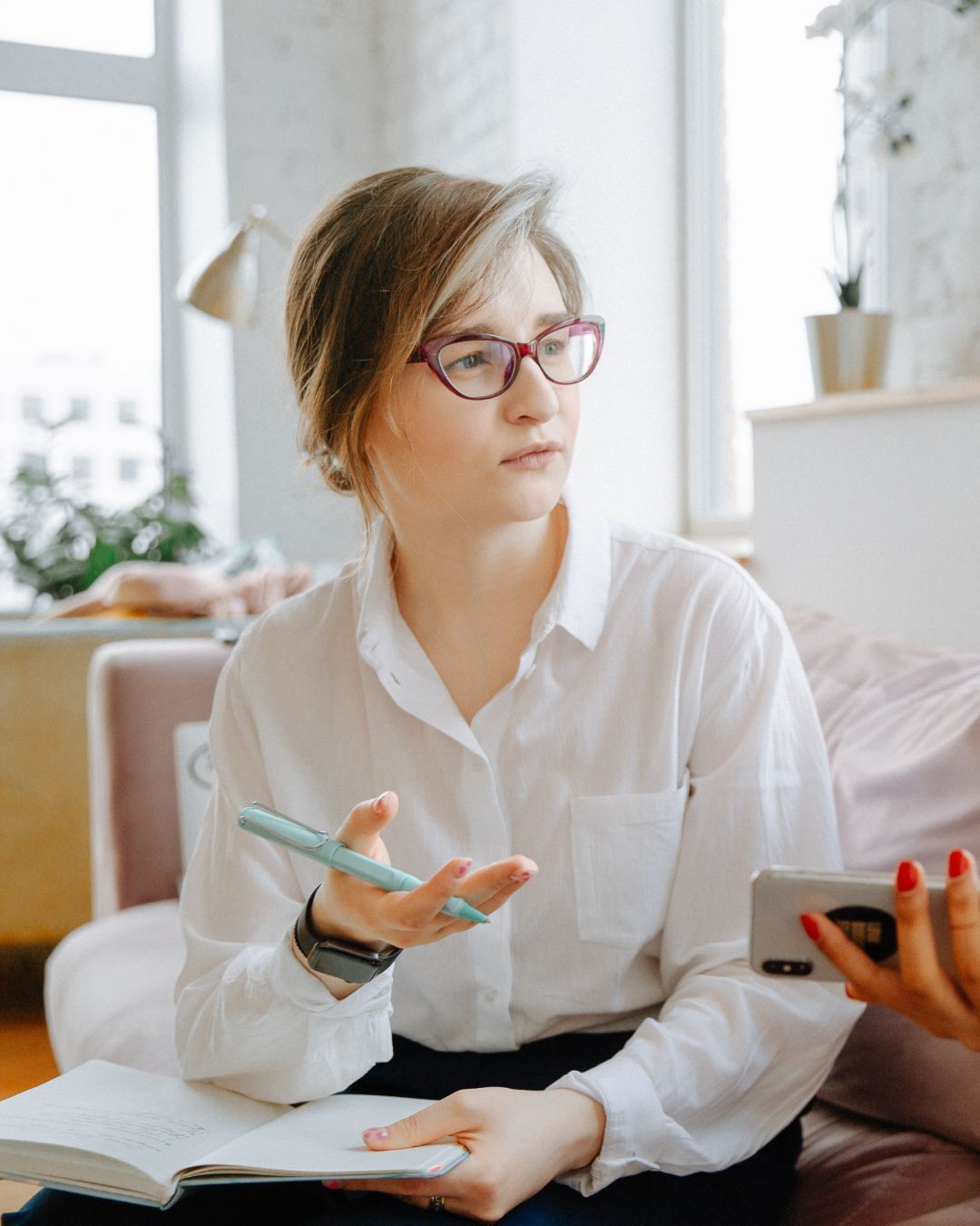 A woman is sitting on a couch holding a pen and a notebook.