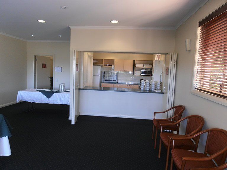 A room with a table and chairs and a kitchen in the background