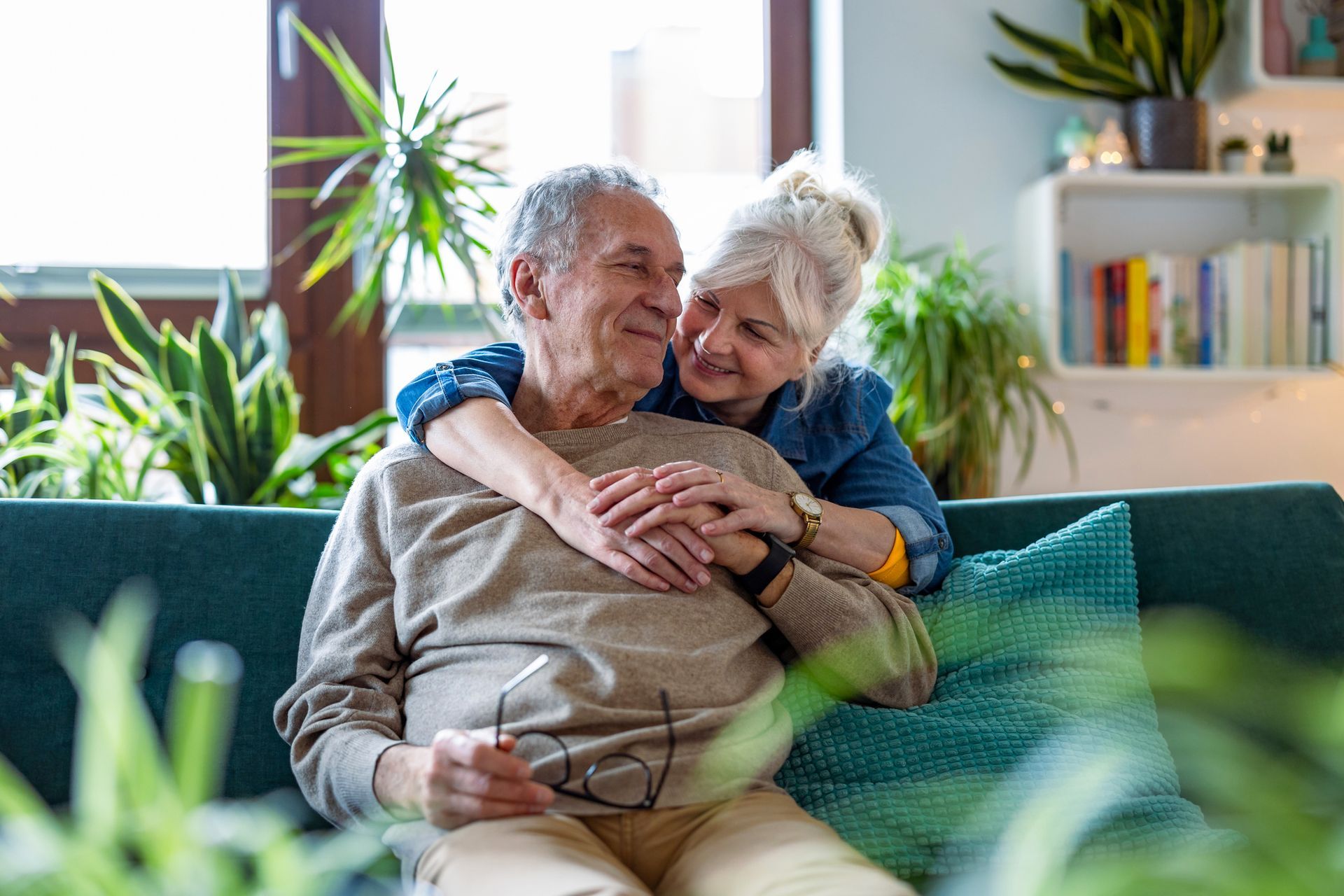 An elderly couple is sitting on a couch hugging each other.
