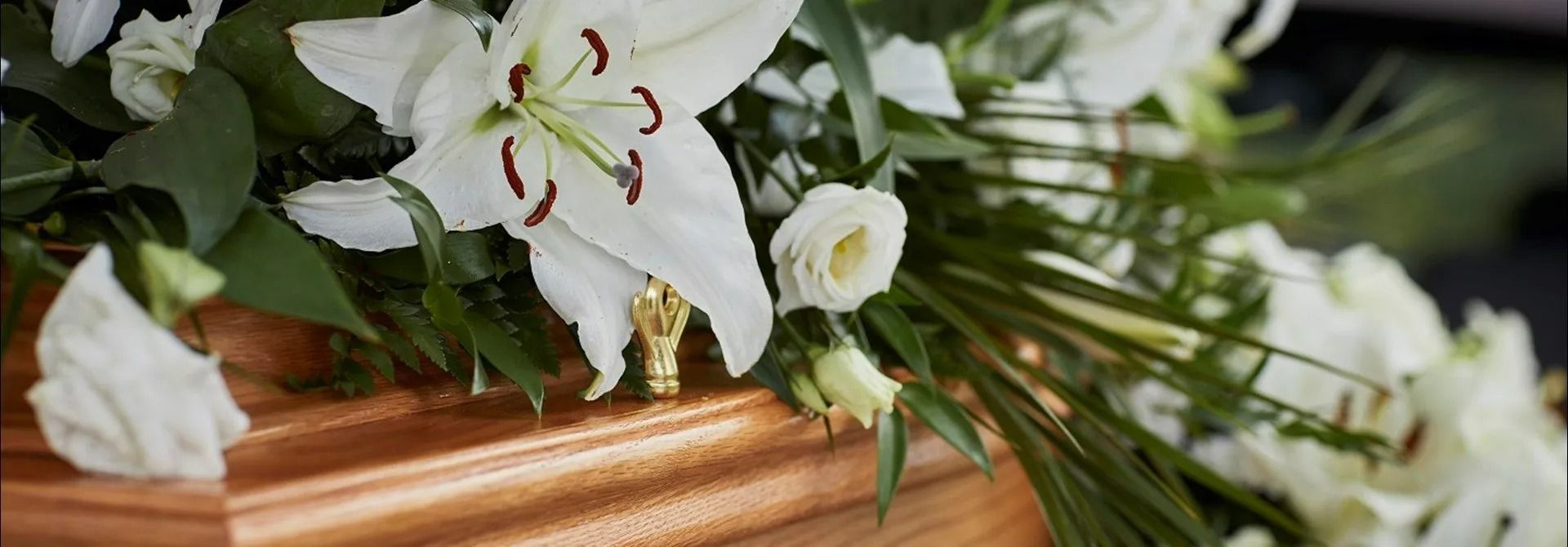 A wooden coffin filled with white flowers and greenery.