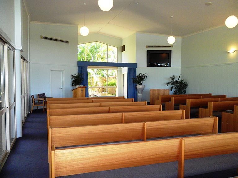 A church with rows of wooden benches and a television on the wall.