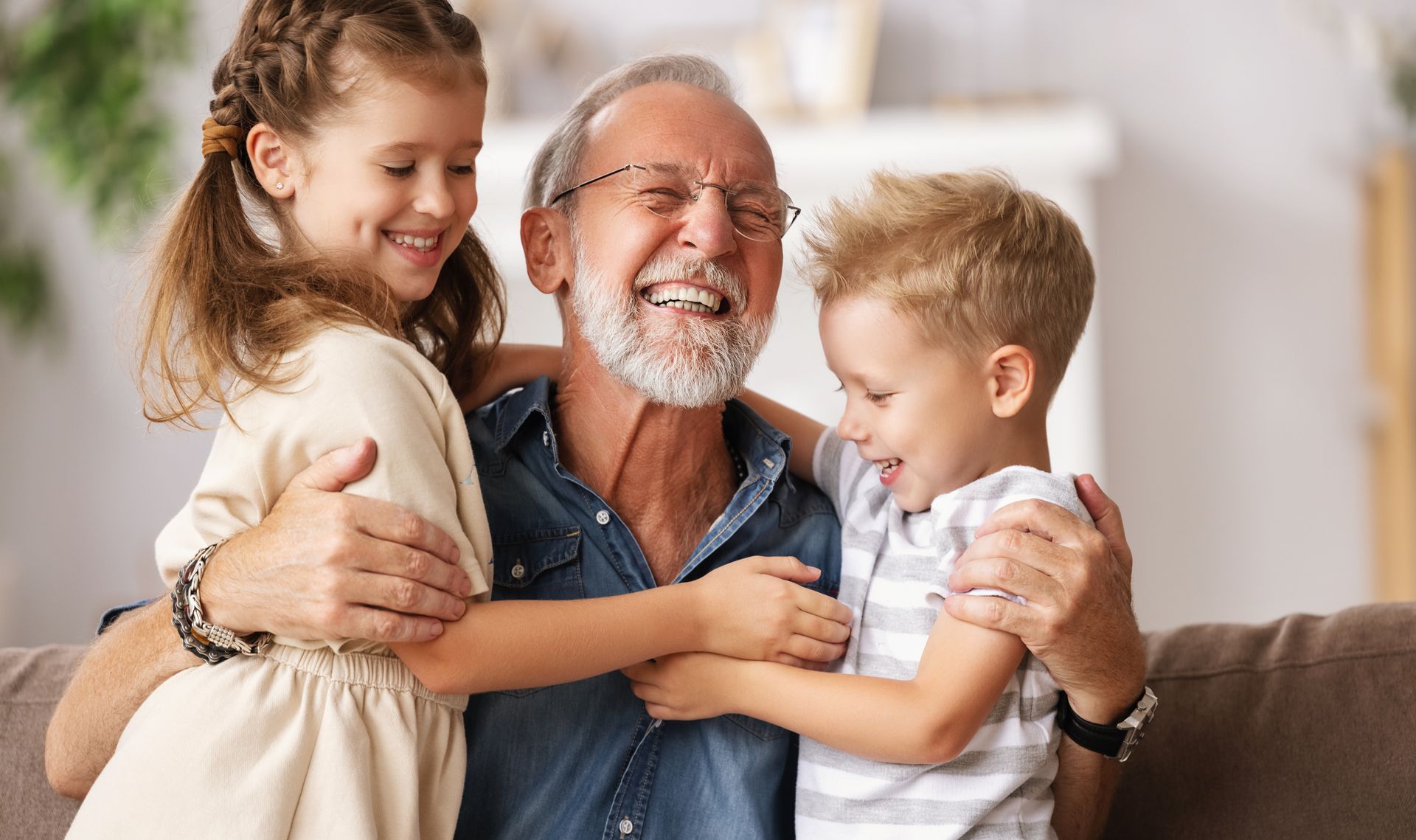 An elderly man is sitting on a couch with two children.