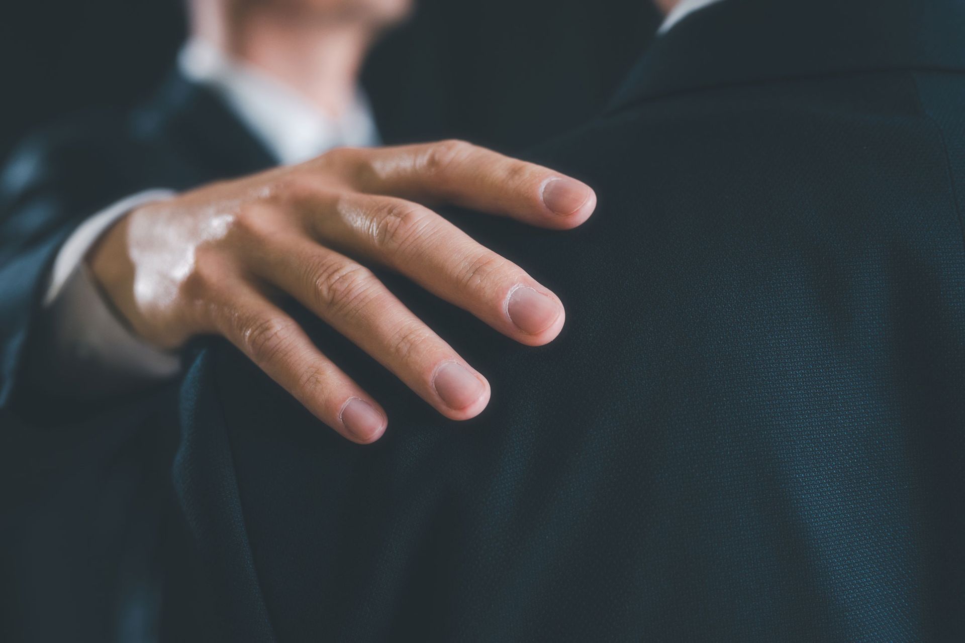 A man in a suit has his hand on his shoulder.