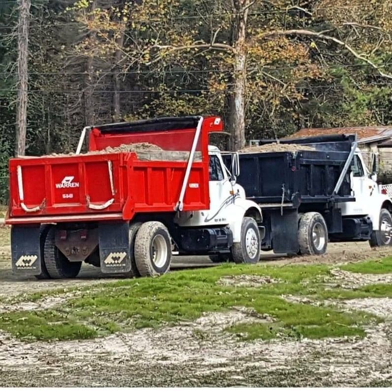 Two dump trucks are parked next to each other in a grassy field