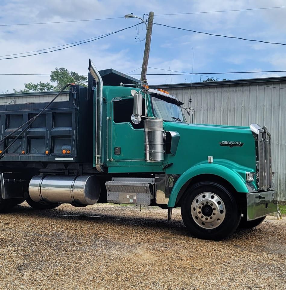 A green dump truck is parked in a gravel lot