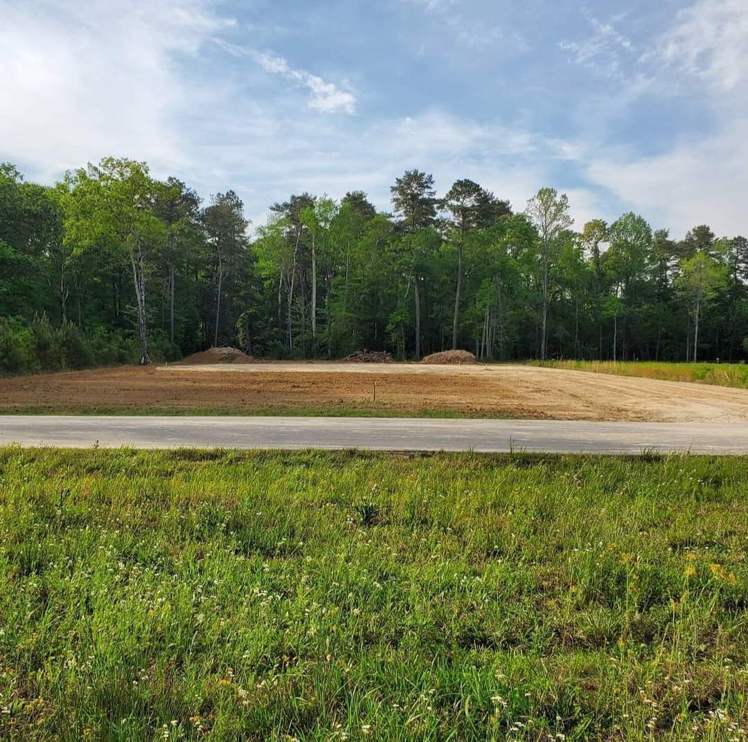 A large grassy field with trees in the background and a road in the foreground.