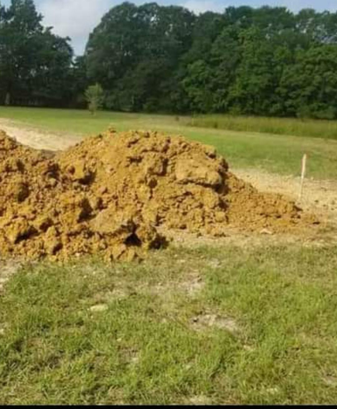A large pile of dirt is sitting in the middle of a grassy field.