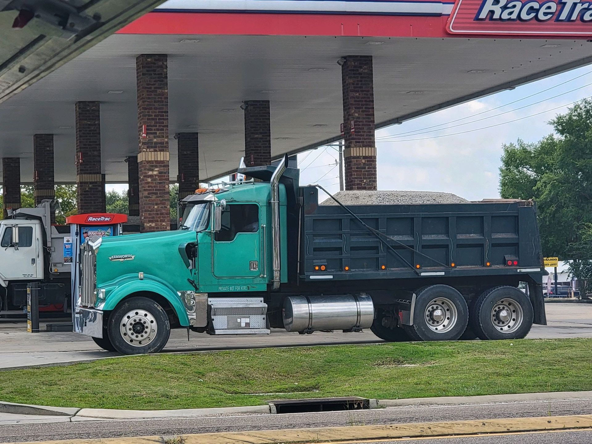 A green dump truck is parked in front of a race track gas station