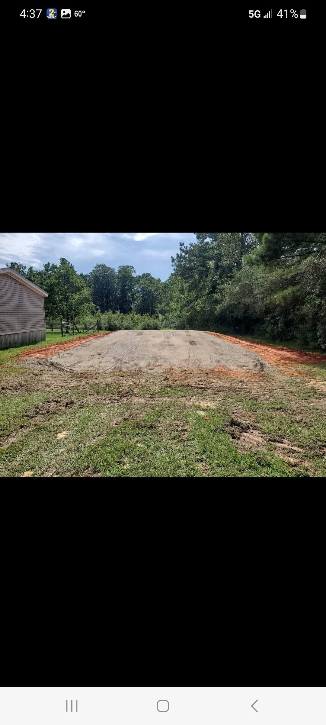A dirt road going through a grassy field with a house in the background.