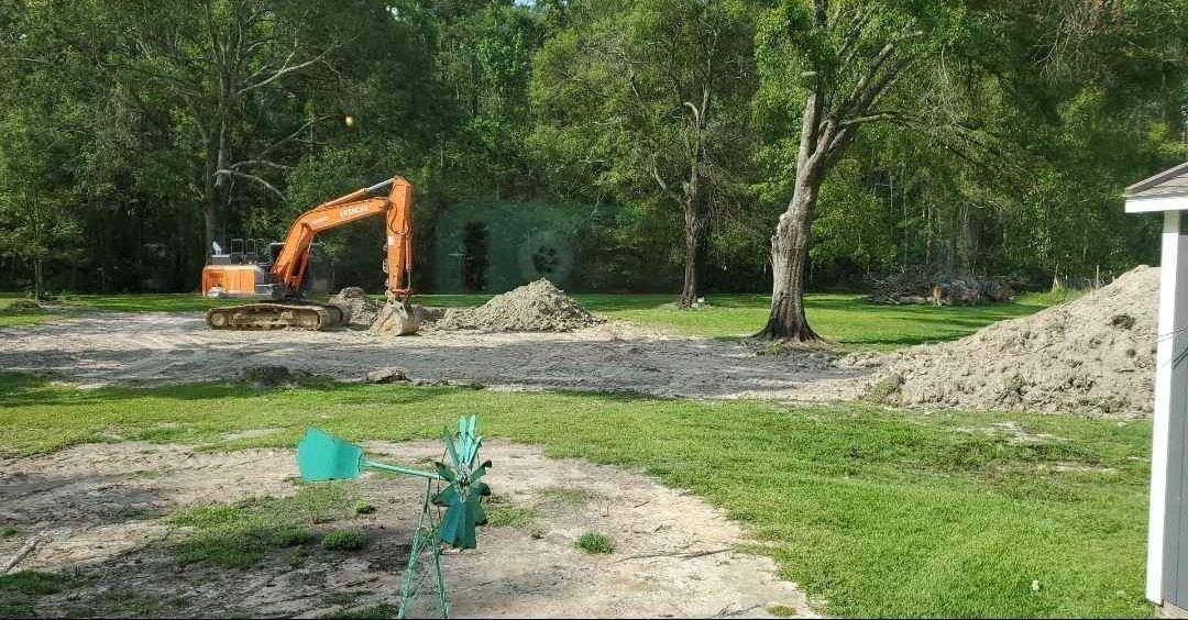An excavator is moving dirt in a yard next to a house.