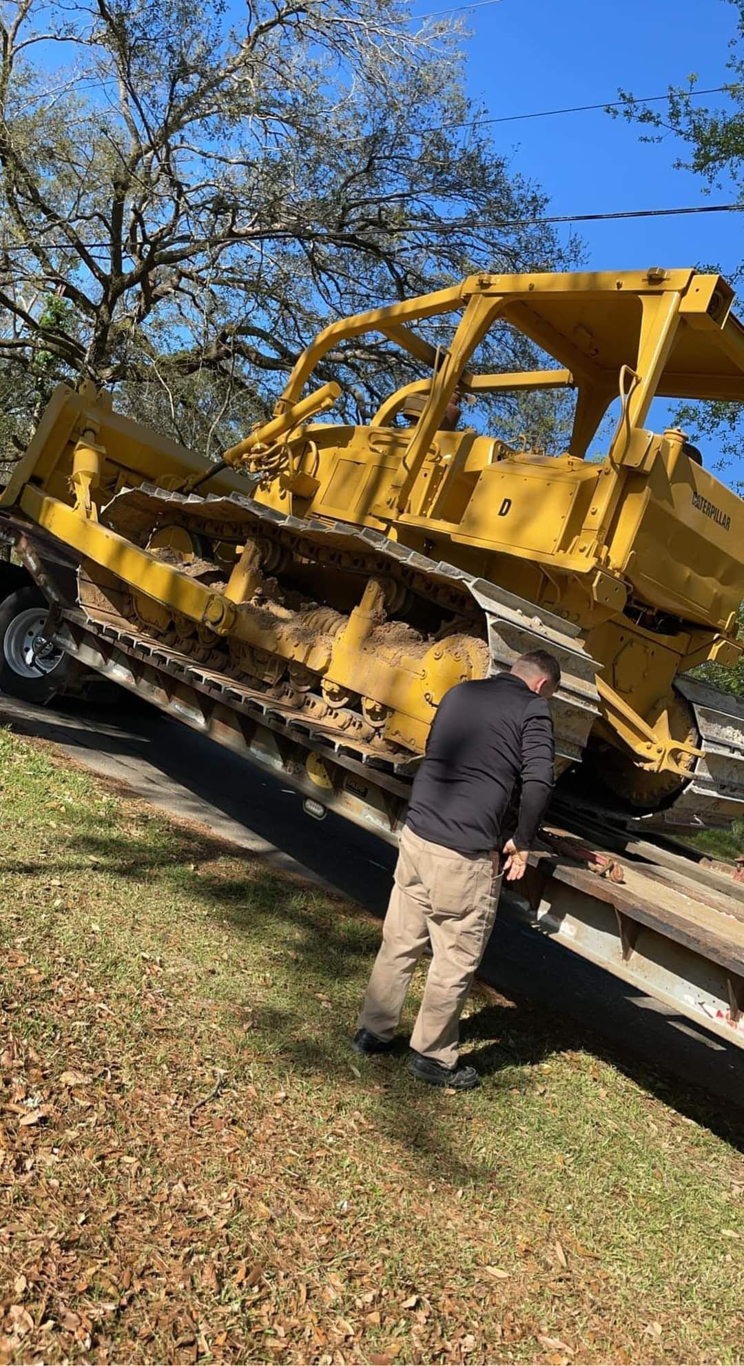A man is standing next to a yellow bulldozer on a trailer.