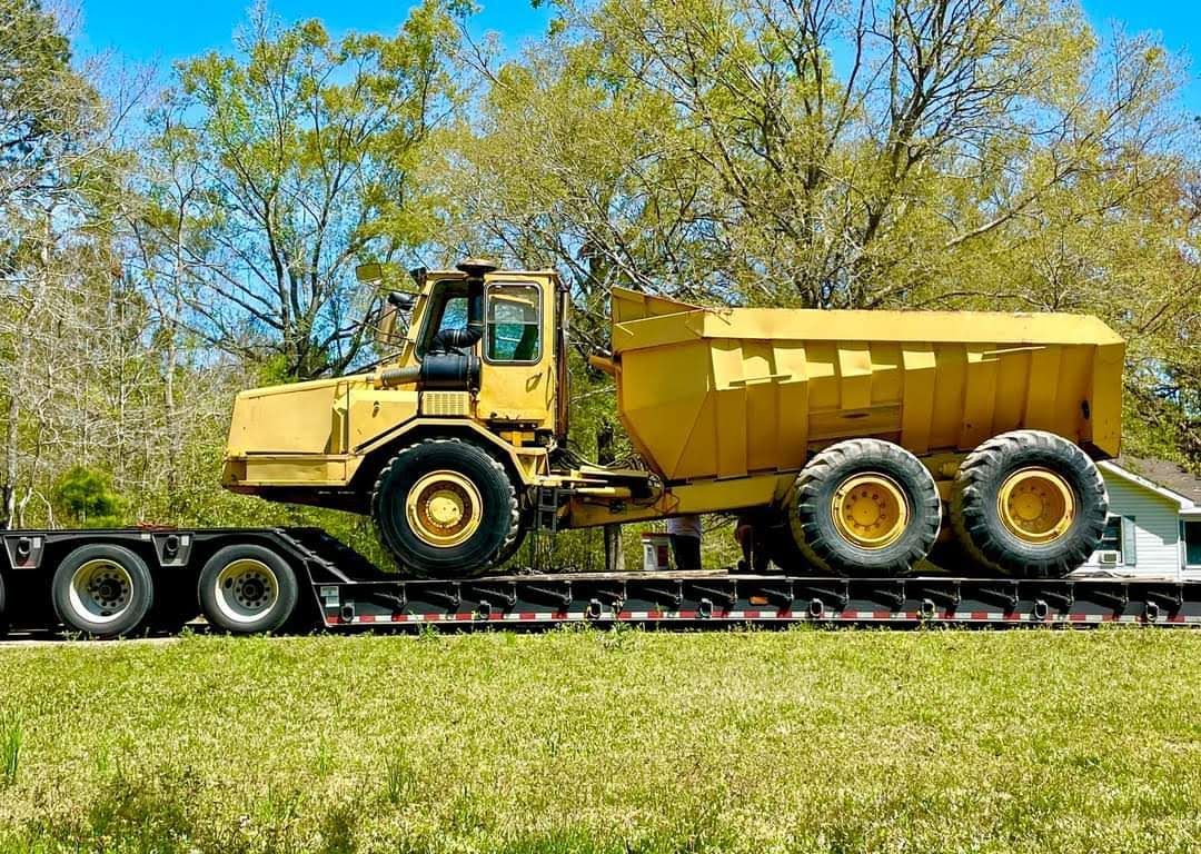 A yellow dump truck is sitting on top of a trailer.