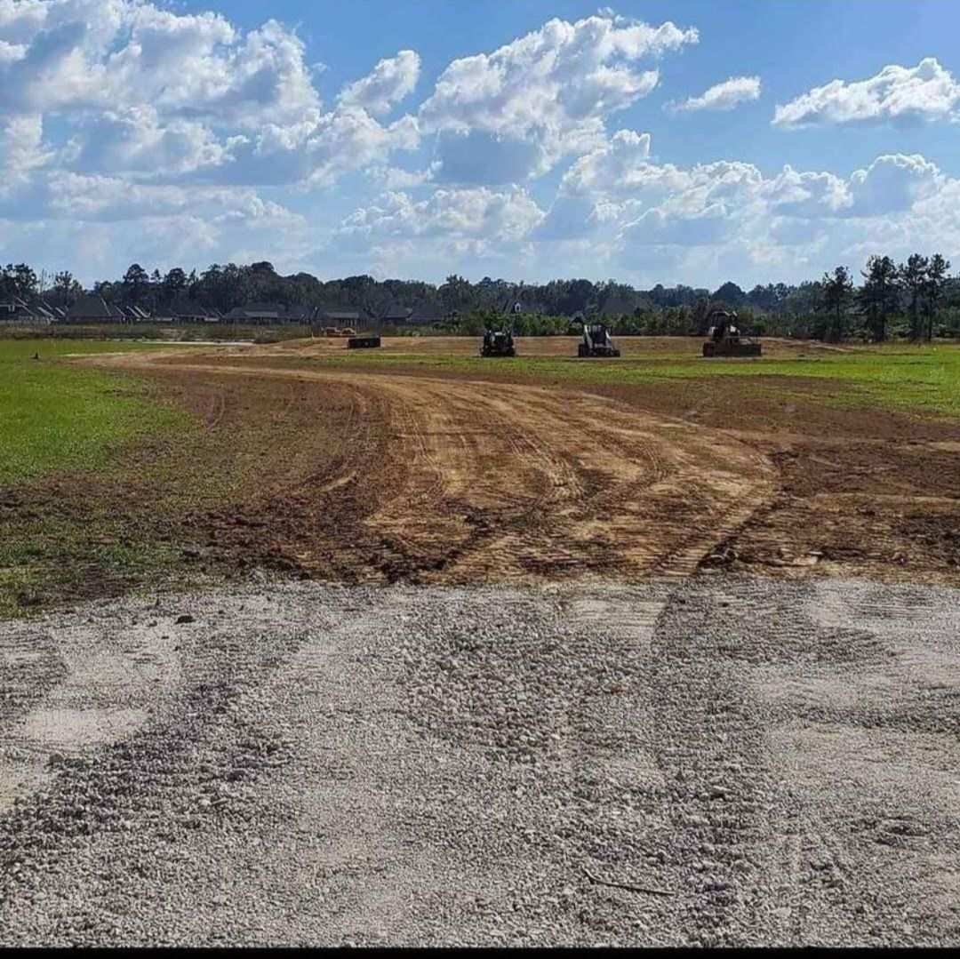 A dirt road going through a grassy field with tractors in the background.