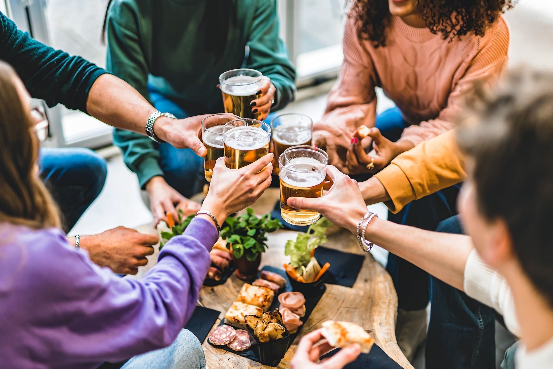 Friends toasting with beer glasses around a table with snacks.