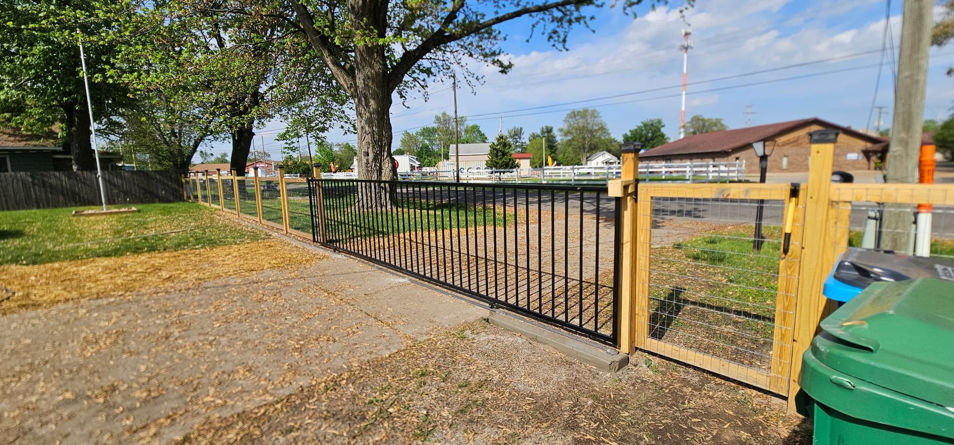 Man in blue shirt and gloves attaching wire fencing to a brown metal post outdoors.