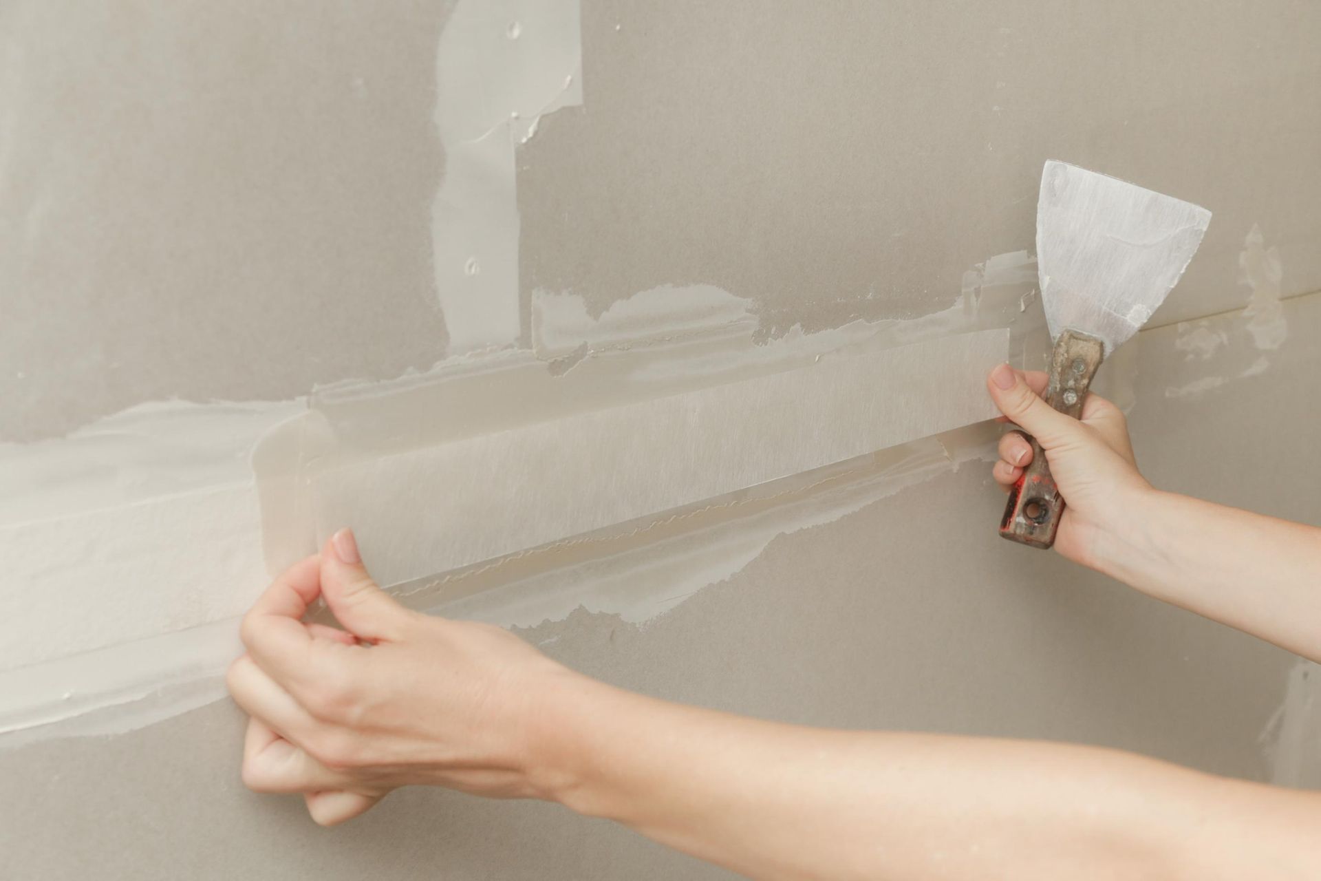 Person applying joint compound to drywall tape with a putty knife.