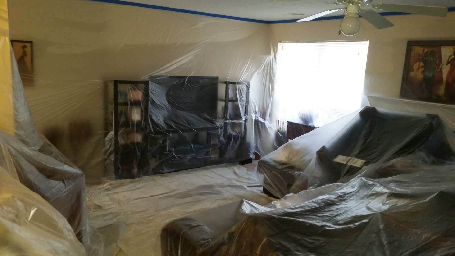 Room covered in plastic sheeting, likely for painting or renovation. Furniture and walls obscured.