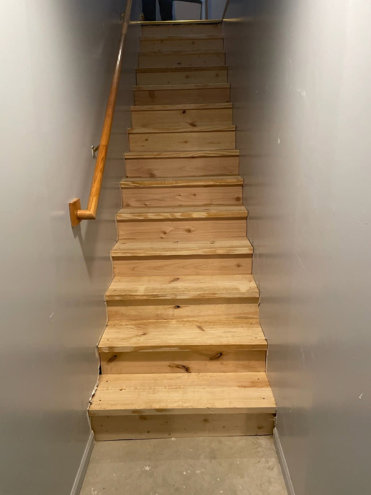Wooden staircase with a handrail in a gray-walled space.