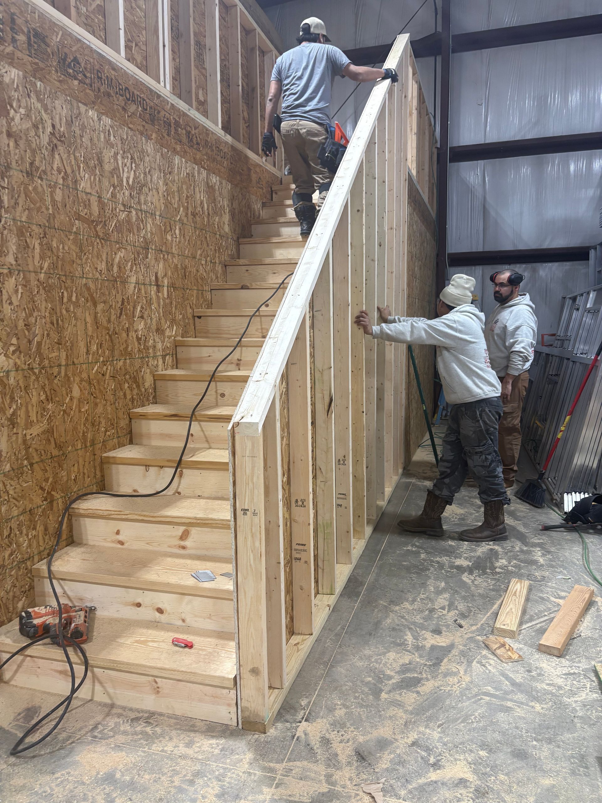 Construction workers framing staircase in a building. Two are on the stairs, one working on the wall.