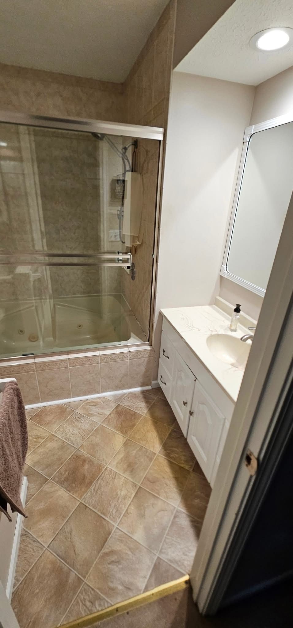 Bathroom with shower, vanity, and tiled floor.  Beige and white color scheme. Door in the foreground.
