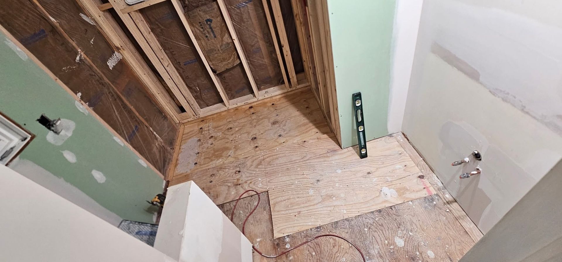 Bathroom under renovation: framing, drywall, and subfloor visible. A level leans against a wall.