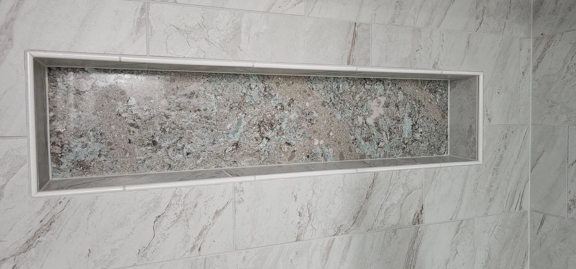 Recessed shower niche with patterned interior, set in gray tiled wall.