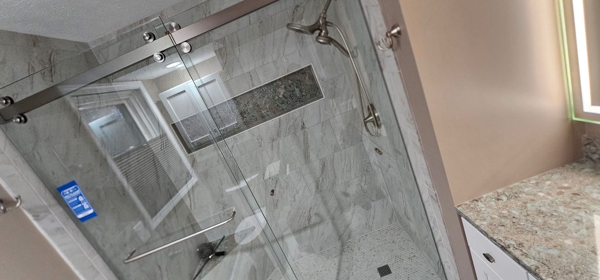 A modern bathroom with a glass shower and stone tile. Light-colored walls and a countertop.