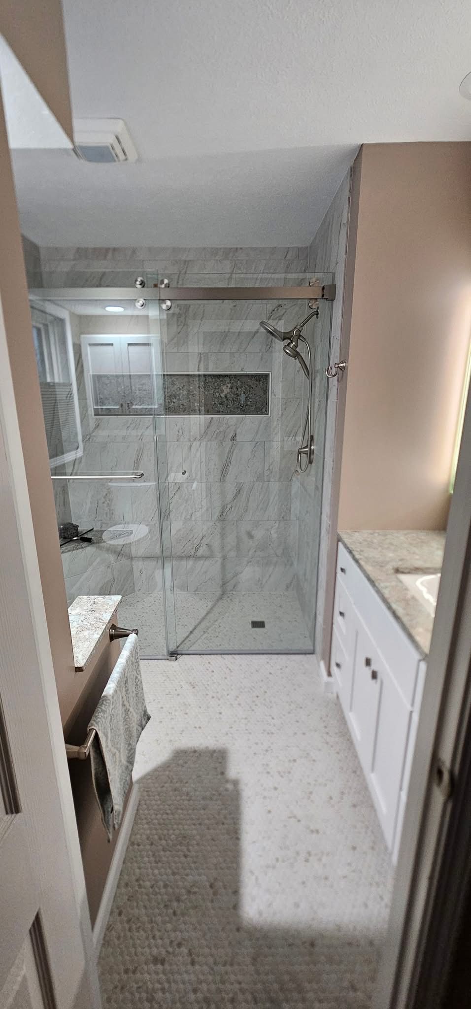 A narrow bathroom with a shower, vanity, and light-colored flooring. The walls are neutral.