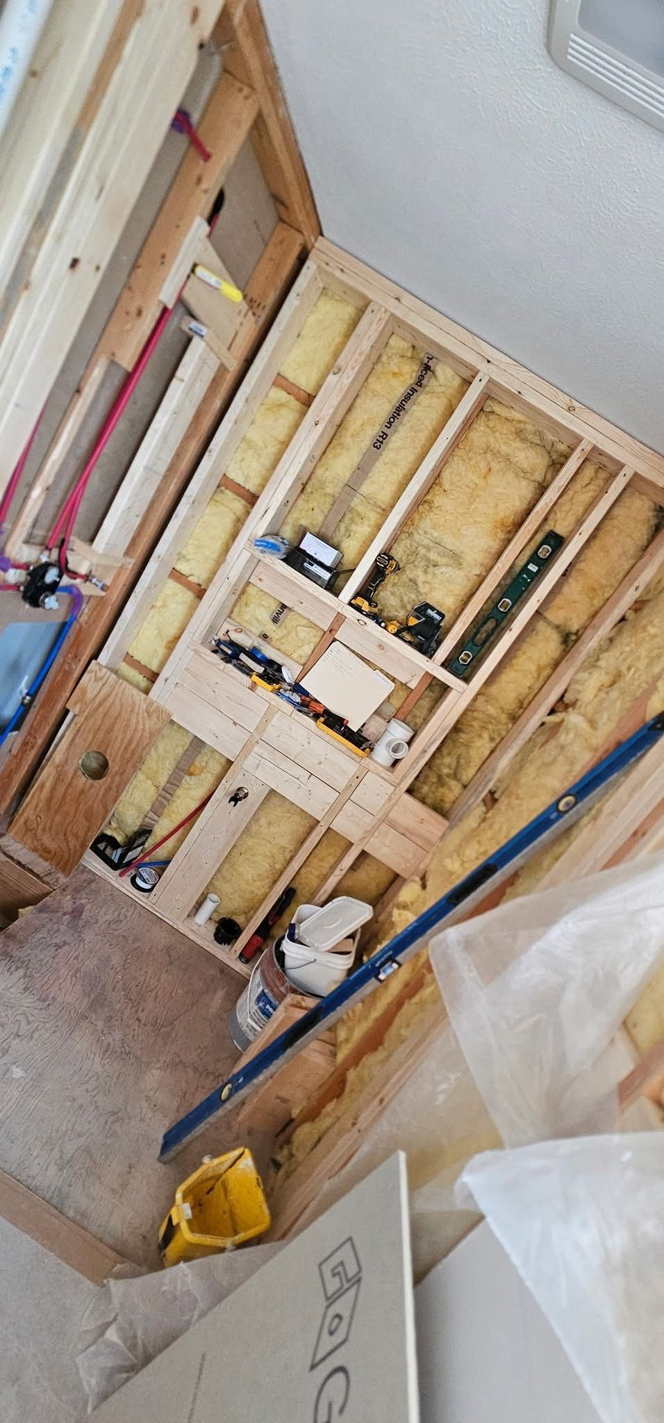 Framed walls with insulation, electrical wiring, and plumbing during a construction project.