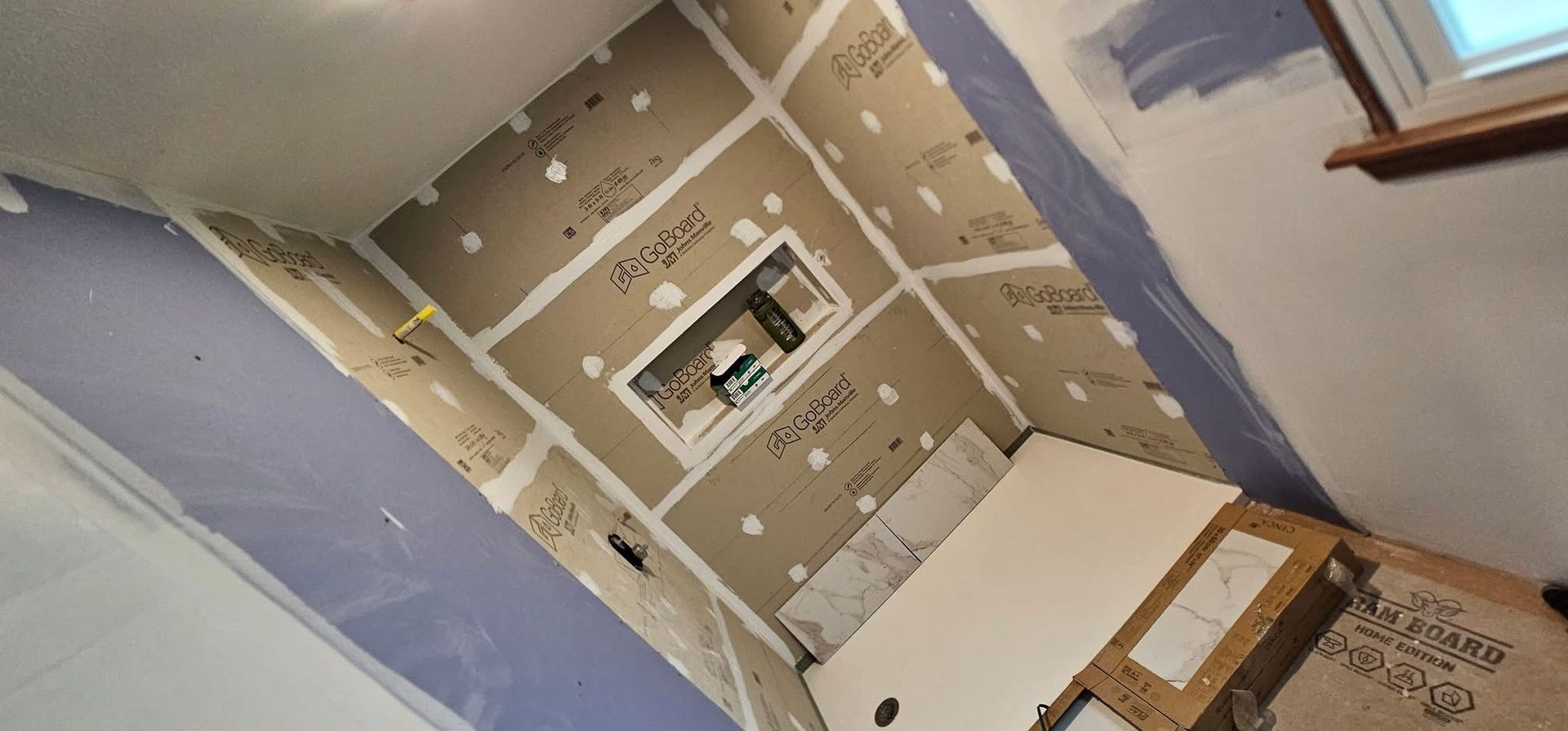 A bathroom under construction with installed drywall and a niche. Walls are covered in cement board.
