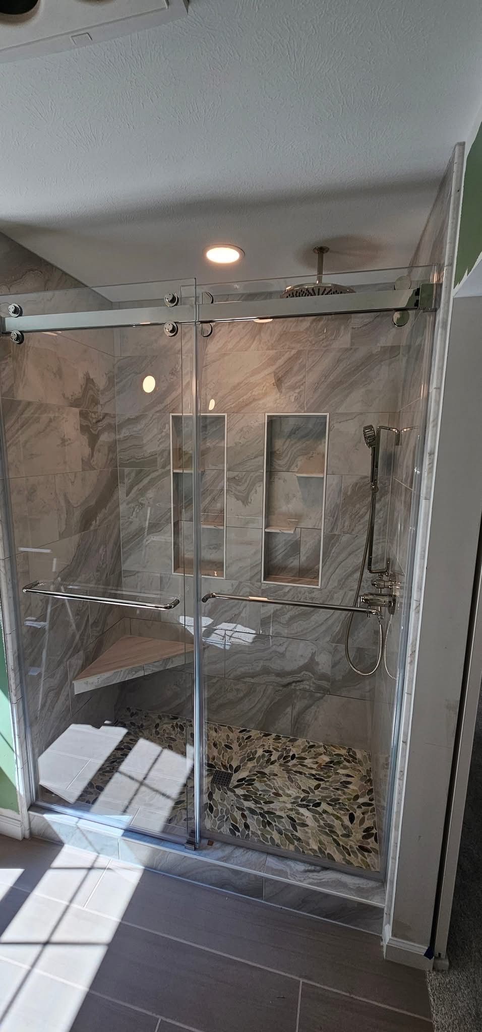 Modern shower with stone tile, glass doors, and river rocks.