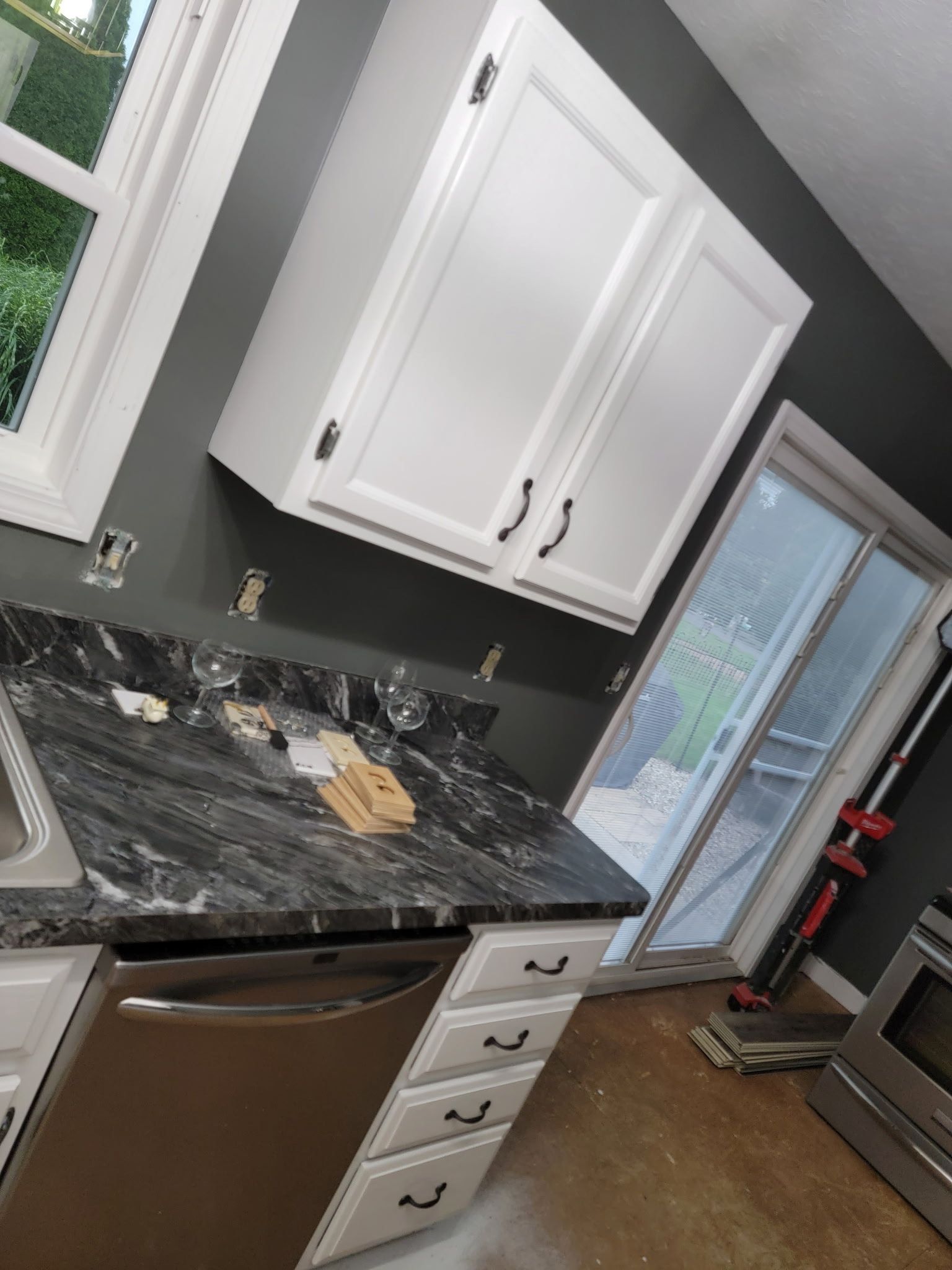 Kitchen with white cabinets, dark countertops, a stainless steel dishwasher, and a sliding glass door.