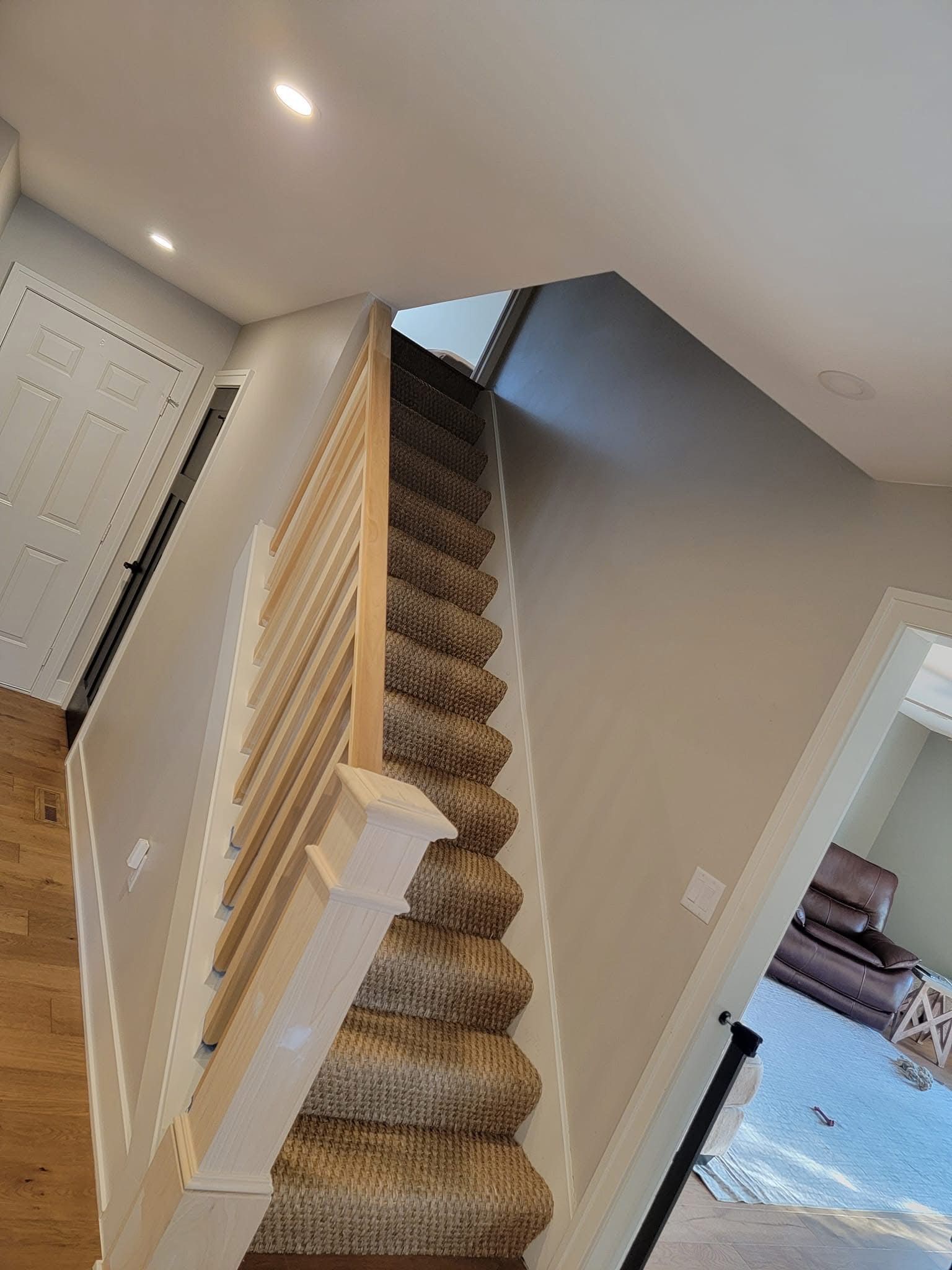 Staircase with carpeted steps and white railing. Light wood floor in the hall, with a door and piano visible.