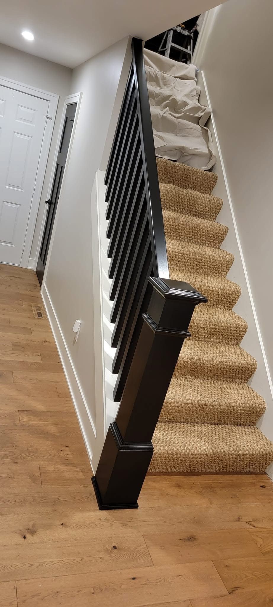 Staircase with carpeted steps and wooden floor; black railing and accents.