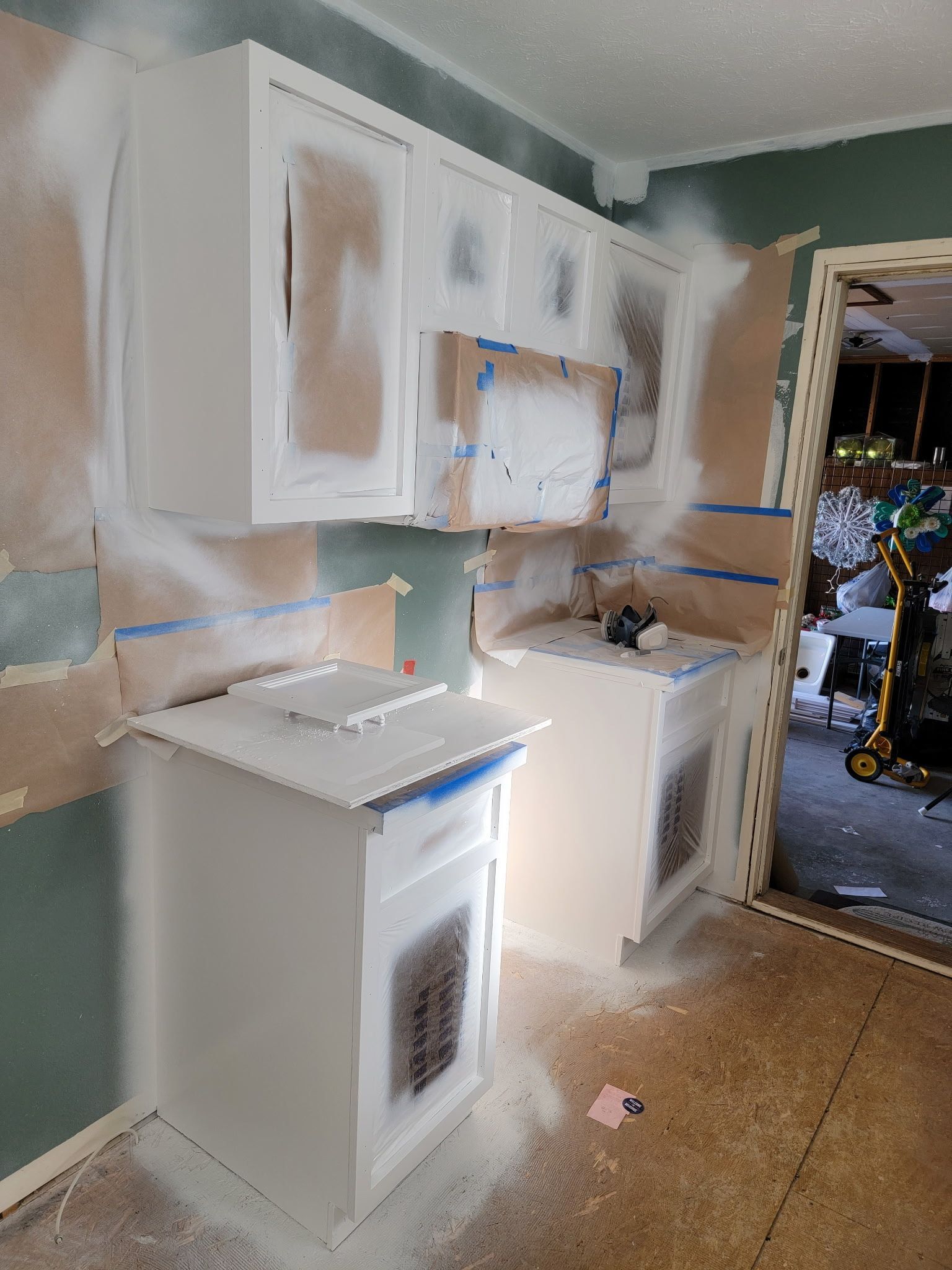 Kitchen cabinets being painted white. Walls are partially covered with masking.