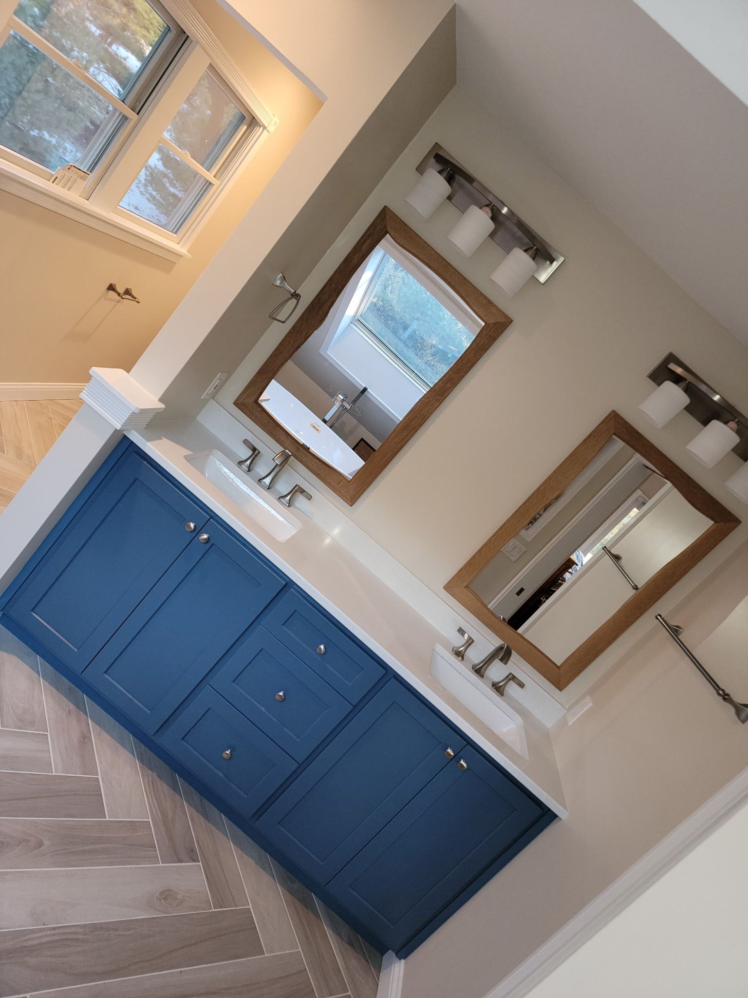 Blue vanity with two sinks, two mirrors, and overhead lights in a bathroom.