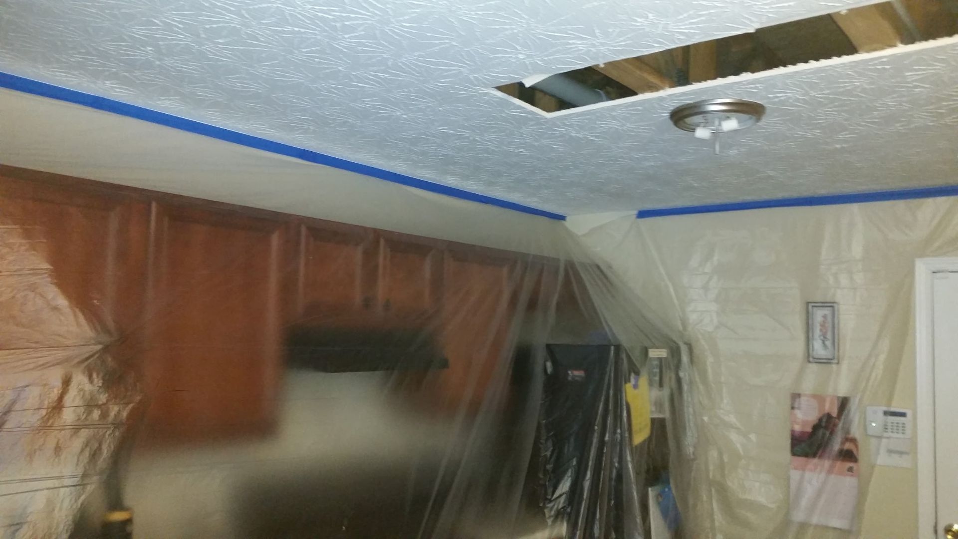 Ceiling with hole, taped trim, plastic sheeting protecting kitchen cabinets, unfinished.