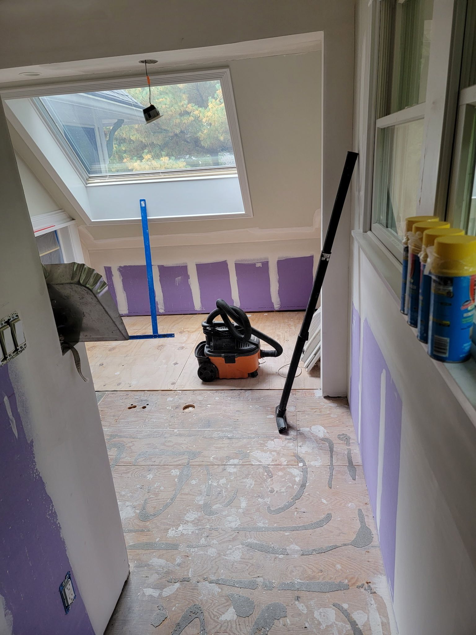 Interior construction site with a vacuum cleaner, a window, and partially installed wallboards.