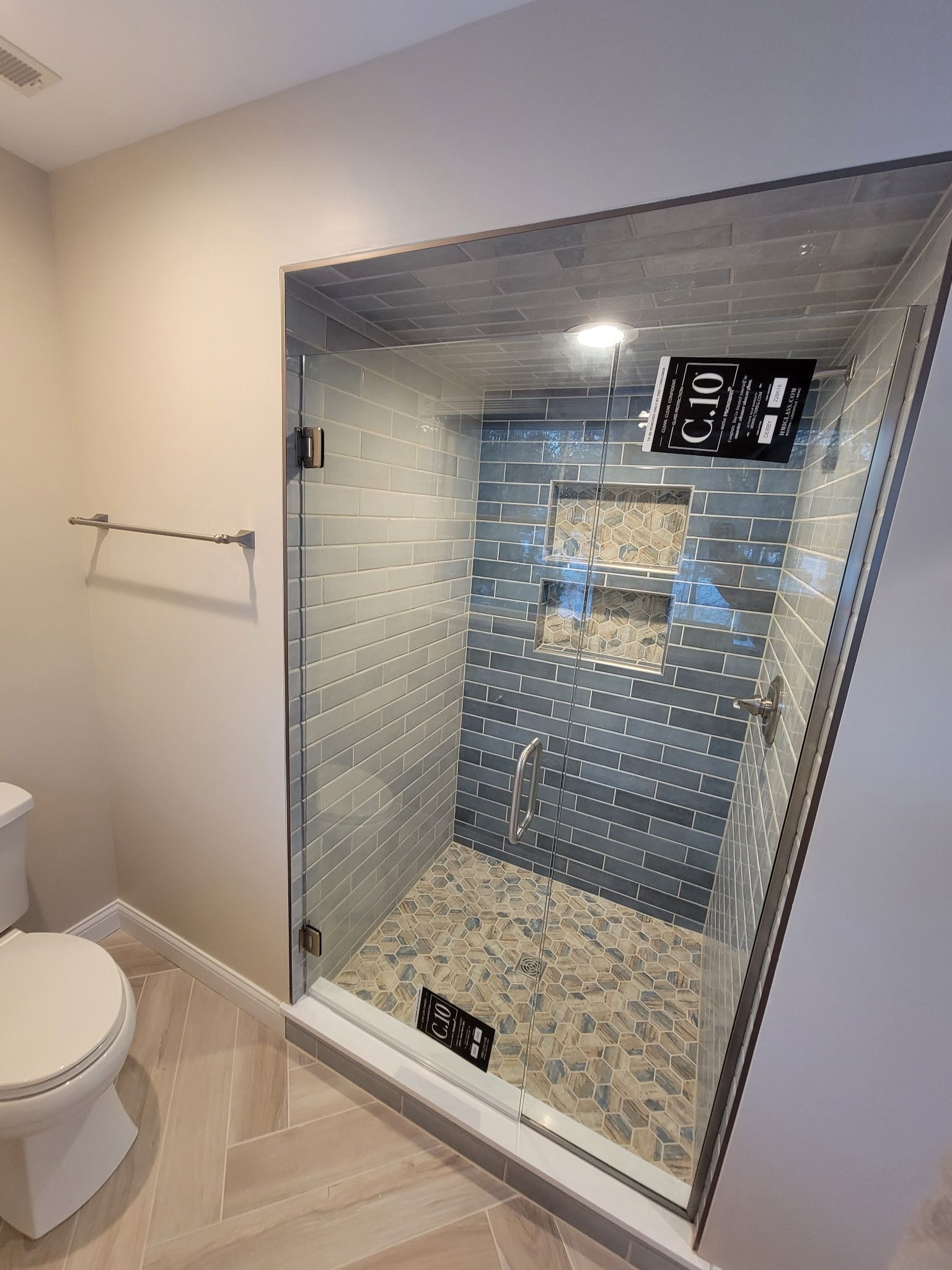 Modern bathroom with glass shower enclosure, pebbled floor, gray and blue tiled walls, and overhead showerhead.